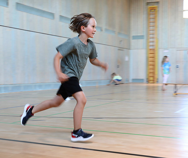 Kleiner Junge in Sportsachen rennt in der Turnhalle eine Runde