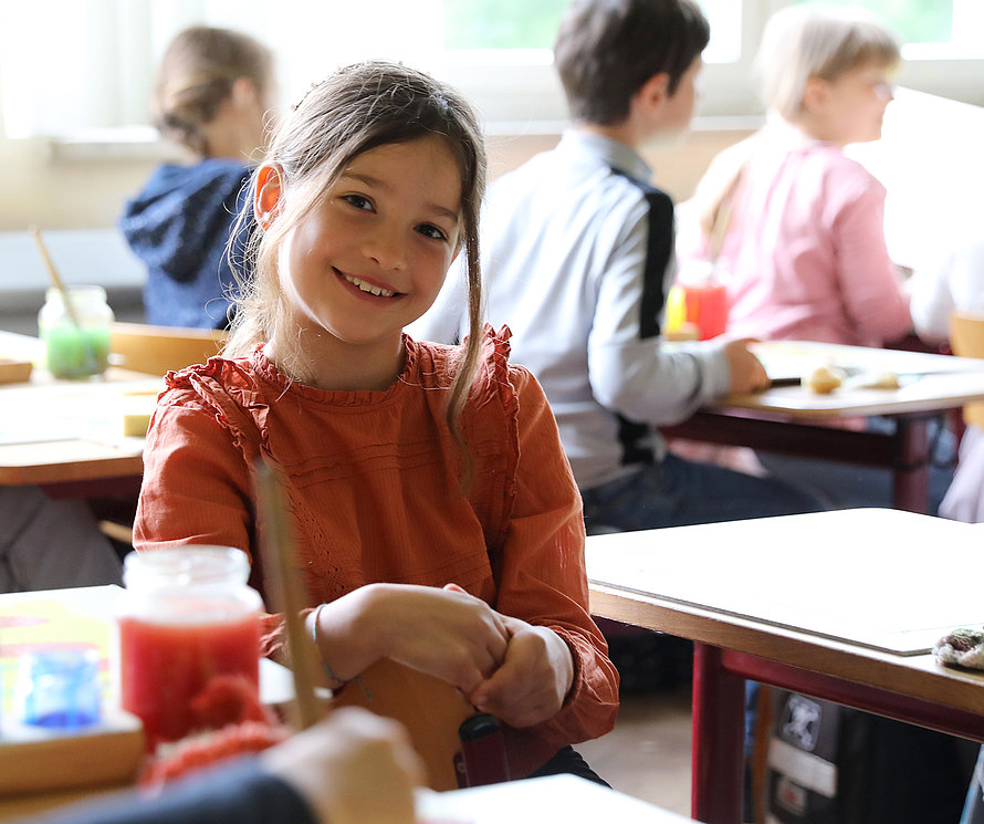 Junges Mädchen sitzt im Klassenzimmer und lächelt in die Kamera