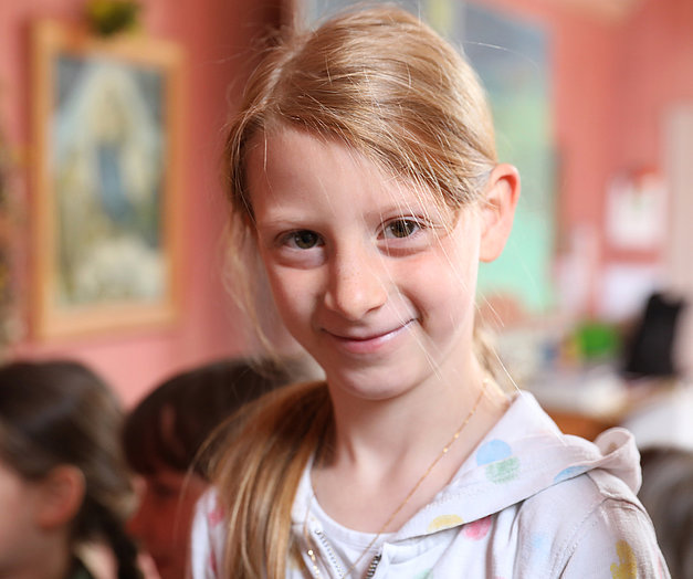 Mädchen mit roten Haaren und Zopf lächelt in die Kamera in einem Klassenzimmer